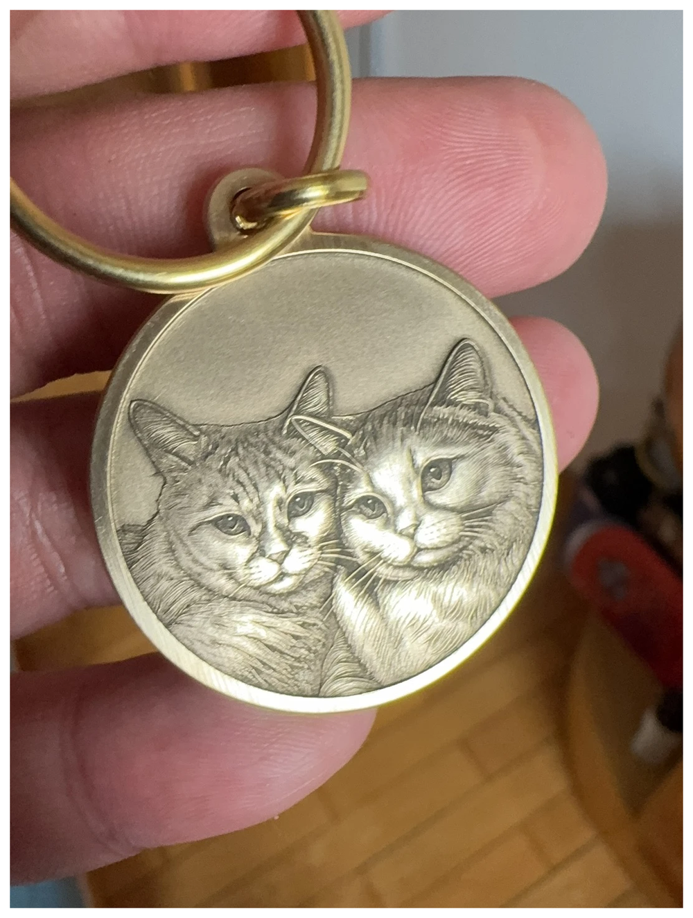 A hand holding a brass keepsake engraved with two cat portraits